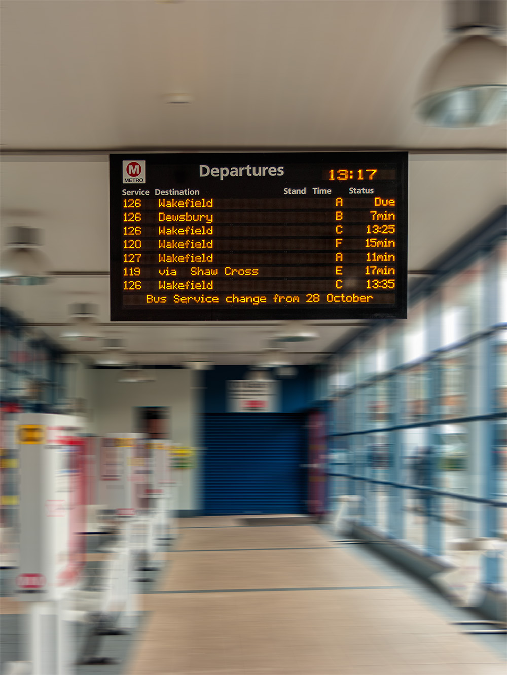 Bus station departure screen shows real time and scheduled departures from different stands. Background is a blurred image of entry gates to the bus station.
